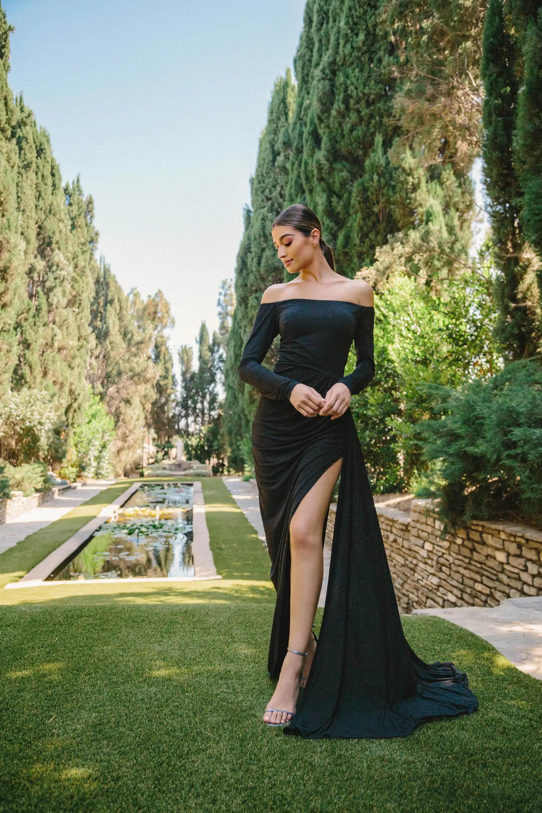 Model wearing a long black evening gown standing at the garden