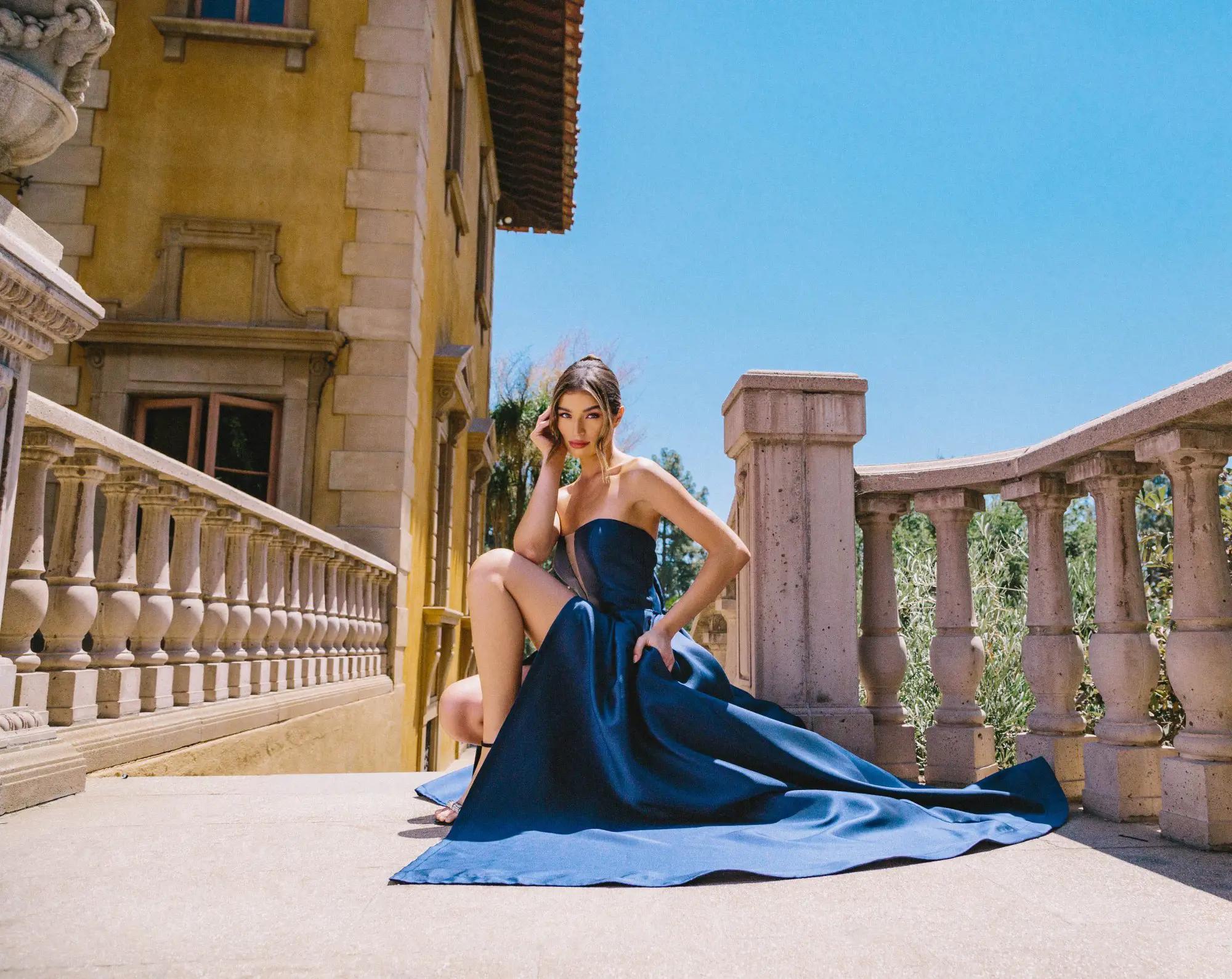 Model wearing a long dark blue evening gown sitting on the floor