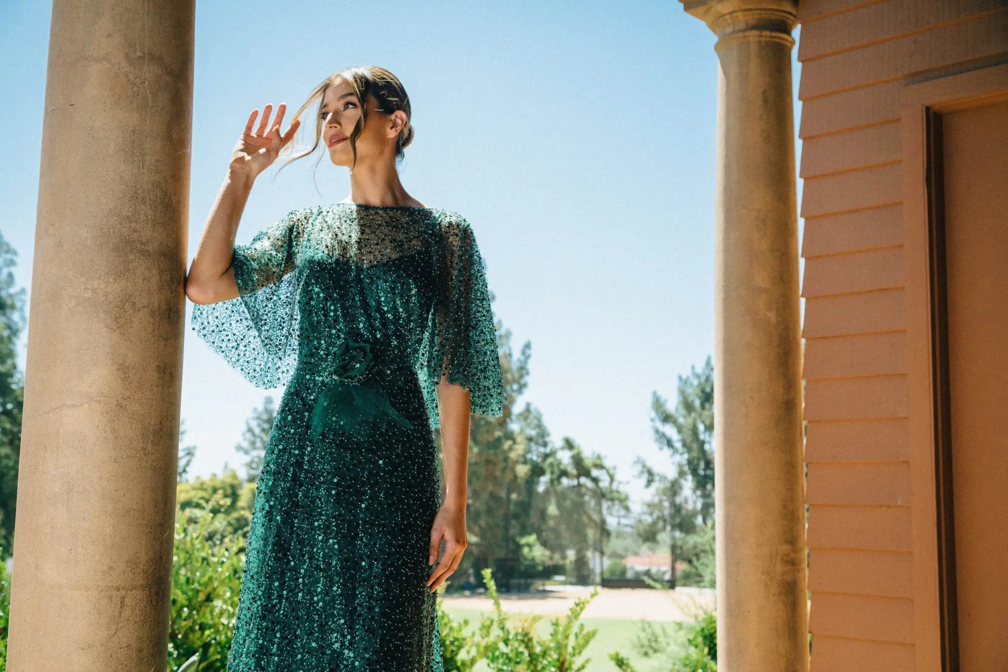 Model wearing a long green evening gown near the garden