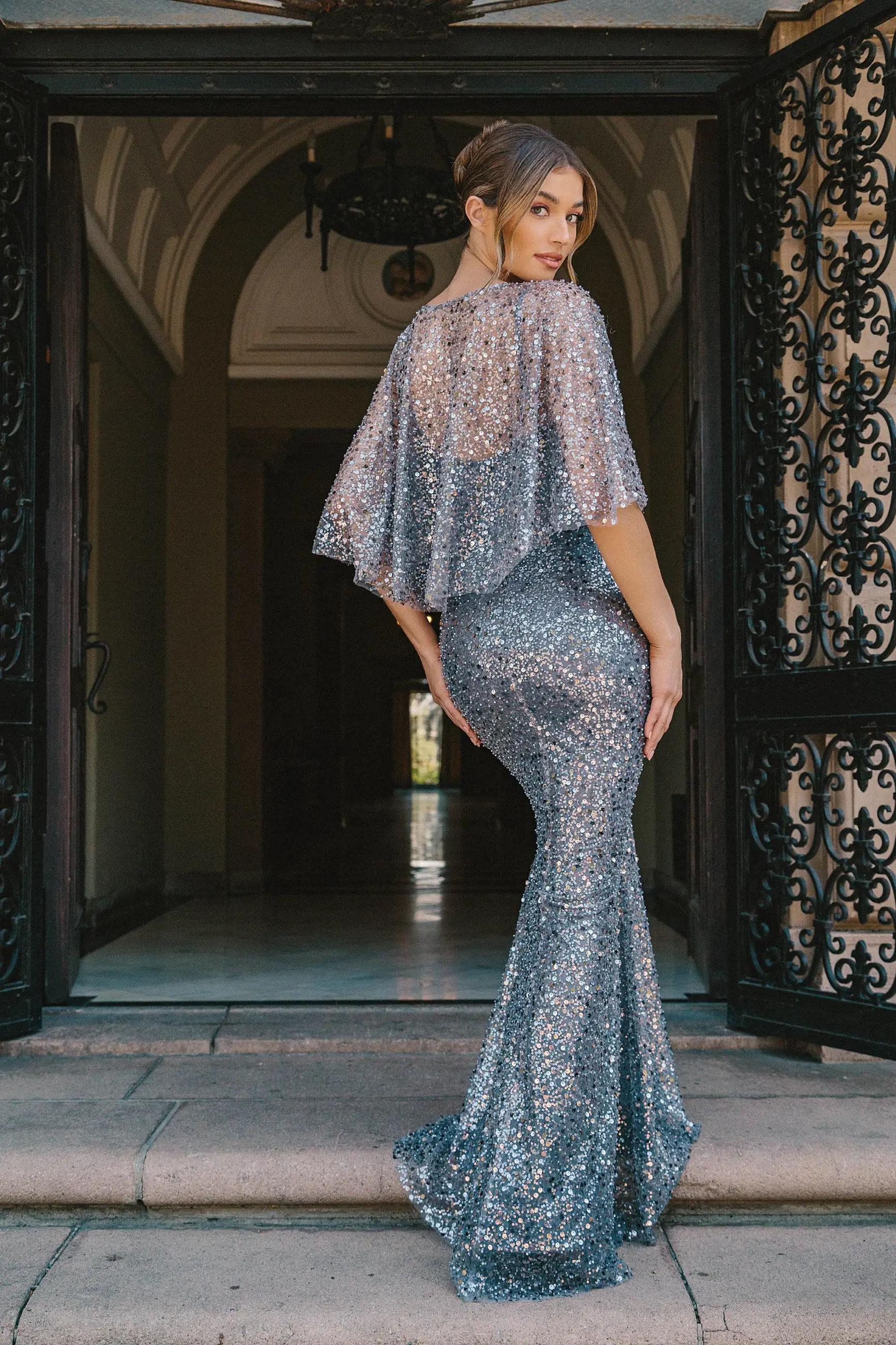 Model wearing a long silver evening gown near the building