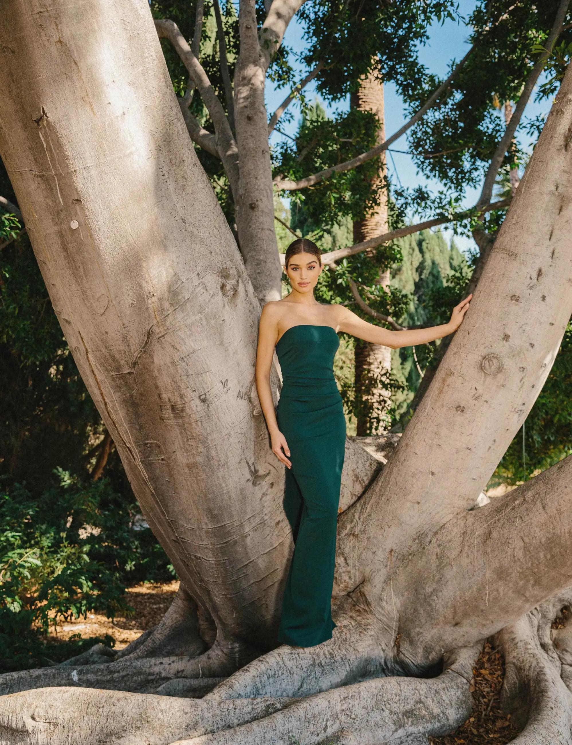 Model wearing a long dark green evening gown posing near the tree
