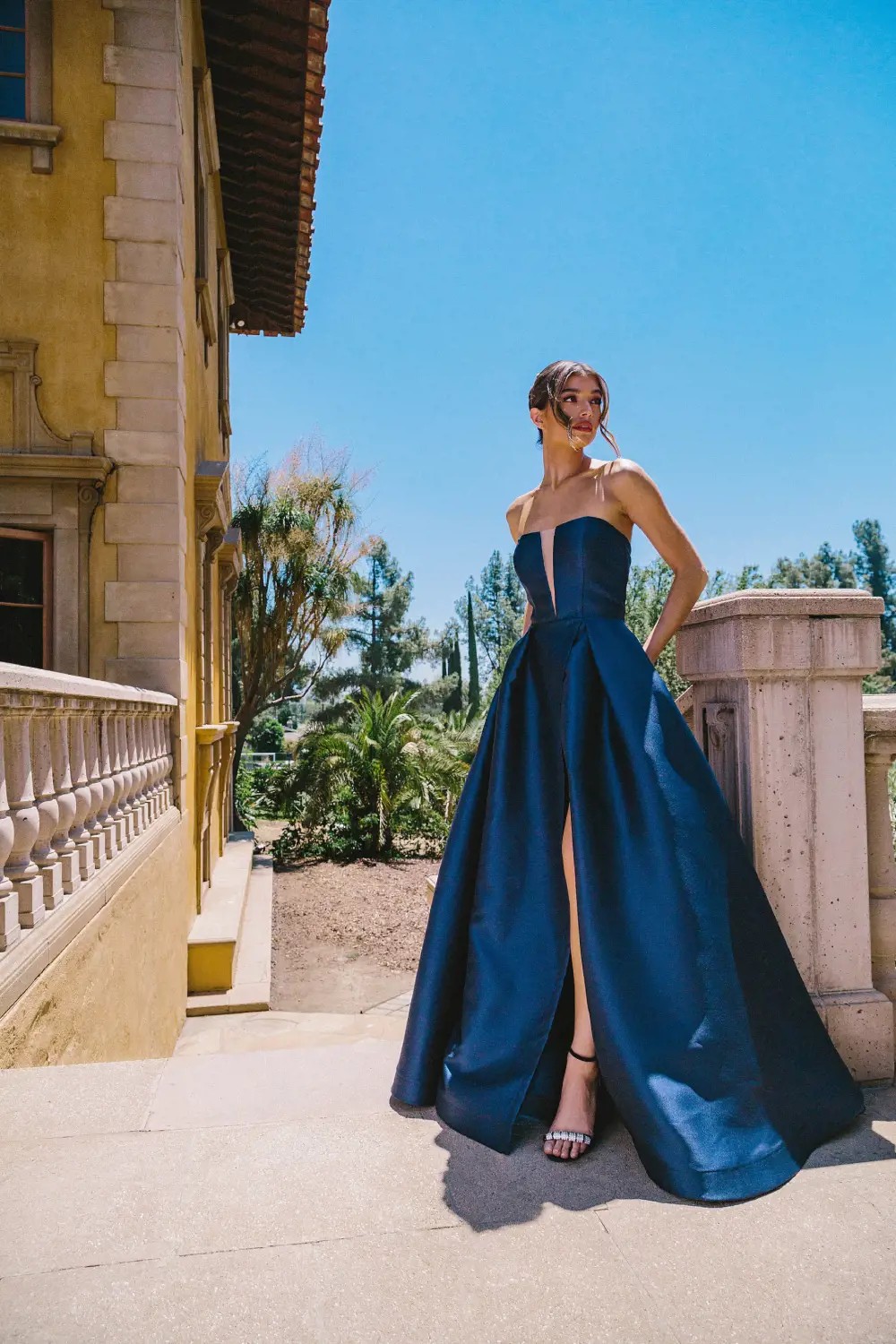 Model wearing a long dark blue evening gown near the garden